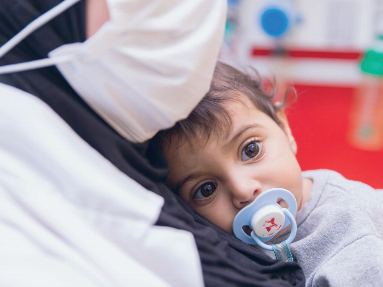Mutter mit Maske und Baby im Caritas Baby Hospital Ein krankes Kind auf dem Arm der Mama