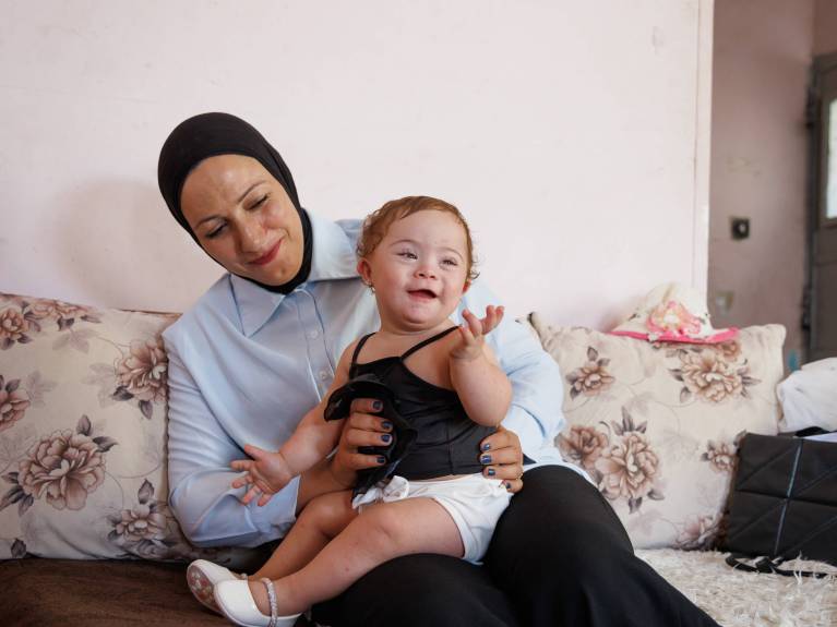 Ein Kind mit Down-Syndrom sitzt auf dem Schoß seiner Mama