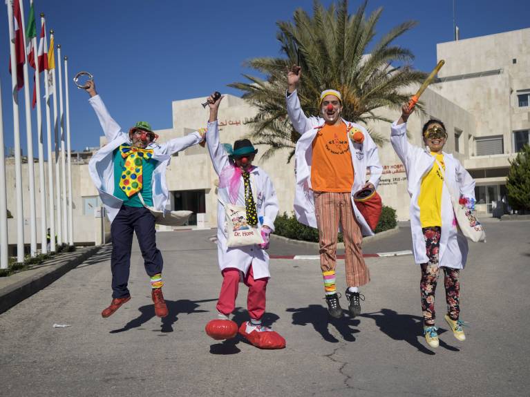 Spital-Clowns - Kinderhilfe Bethlehem Eine Gruppe von Clowns hüpft freudig vor dem Caritas Baby Hospital