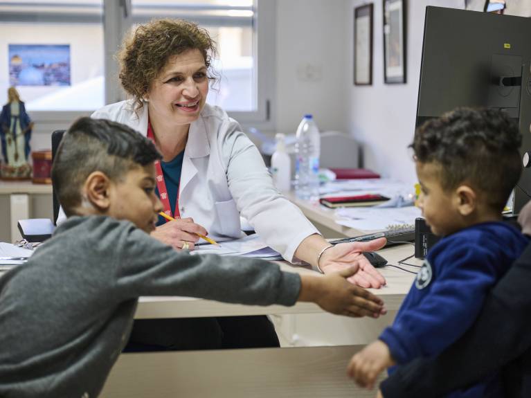 Eine Sozialarbeiterin im Gespräch mit einer Familie Die Sozialarbeiterin spielt mit zwei kleinen Patientinnen und Patienten und gibt traumatisierten Kindern Untersützung