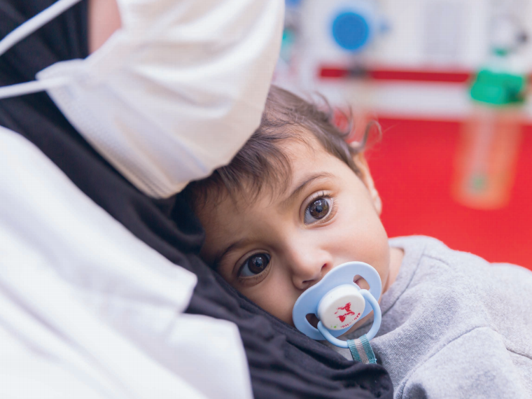 Mutter mit Maske und Baby im Caritas Baby Hospital Ein Kind liegt auf dem Arm seiner Mama