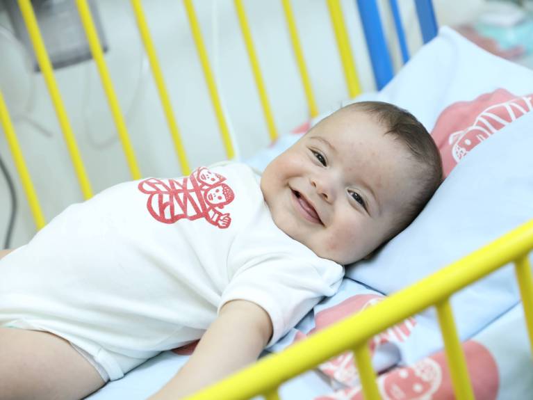 Symbolbild Baby_copyright KHB Ein Baby liegt in der Krippe und lacht